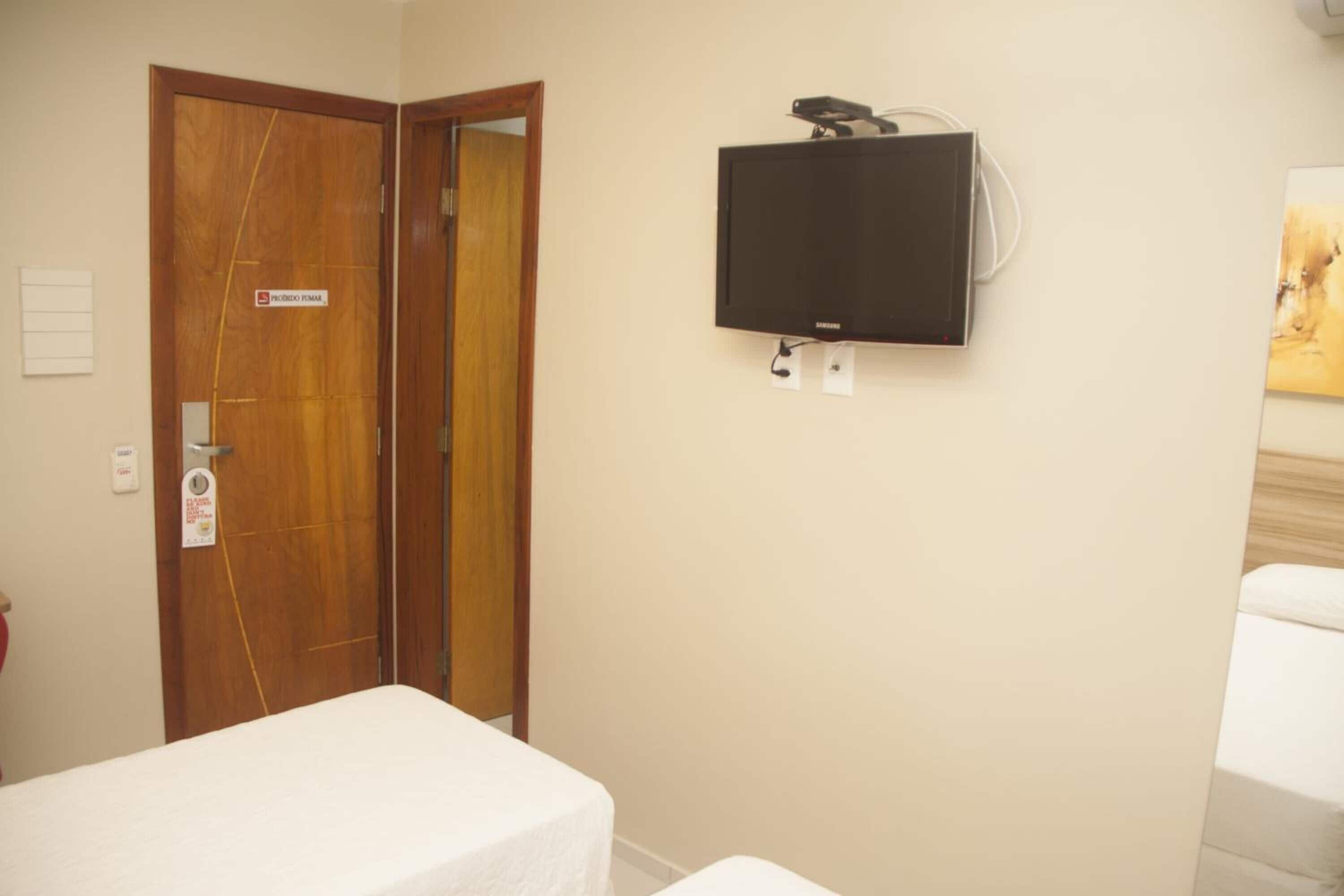 A hotel room with a bed, a television mounted on the wall, and a wooden door.