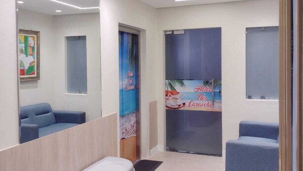 A reception area with a bench, two blue chairs, a large mirror, and a wall with a tropical-themed poster. - Hotel Três Caravelas (Fortaleza)