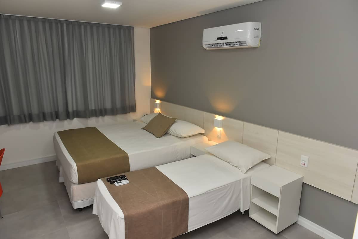 Hotellihuone, jossa on kaksi sänkyä, yöpöytä, seinävalaisin, kaukosäädin ja seinälle asennettu ilmastointilaite.
