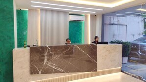 A reception desk with a marble top, two staff members behind it, and a green wall to the left. - Hotel Três Caravelas (Fortaleza)