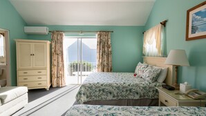 A bedroom with a bed, a nightstand, a lamp, a wardrobe, and a window with curtains. - Dawkins Manor Hotel (Paget Parish)