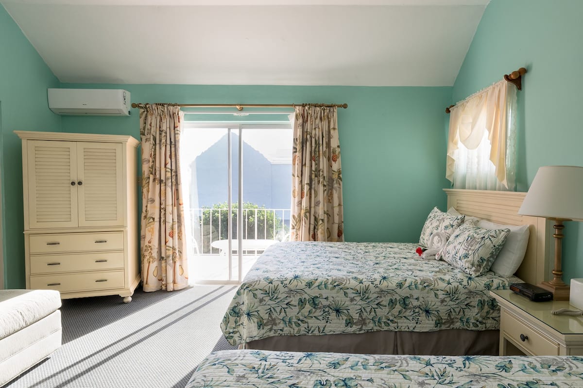 Quarto com cama, mesa de cabeceira, abajur, guarda-roupa e janela com cortinas.