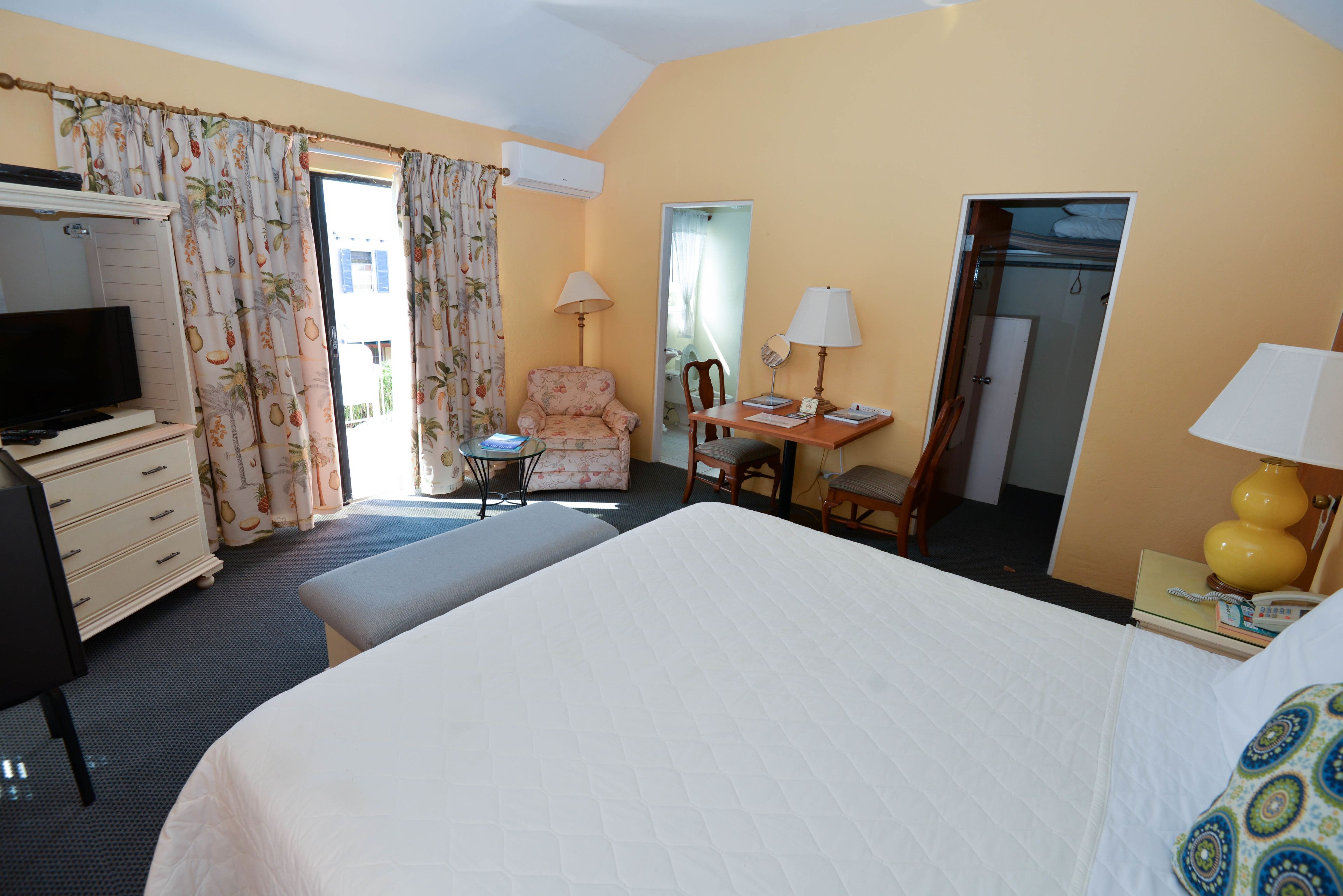 Une chambre d’hôtel comprenant un lit, un bureau avec une chaise, une télévision, une armoire et une porte de salle de bain.