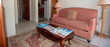 A living room with a red patterned sofa, a coffee table with magazines, and two floor lamps.