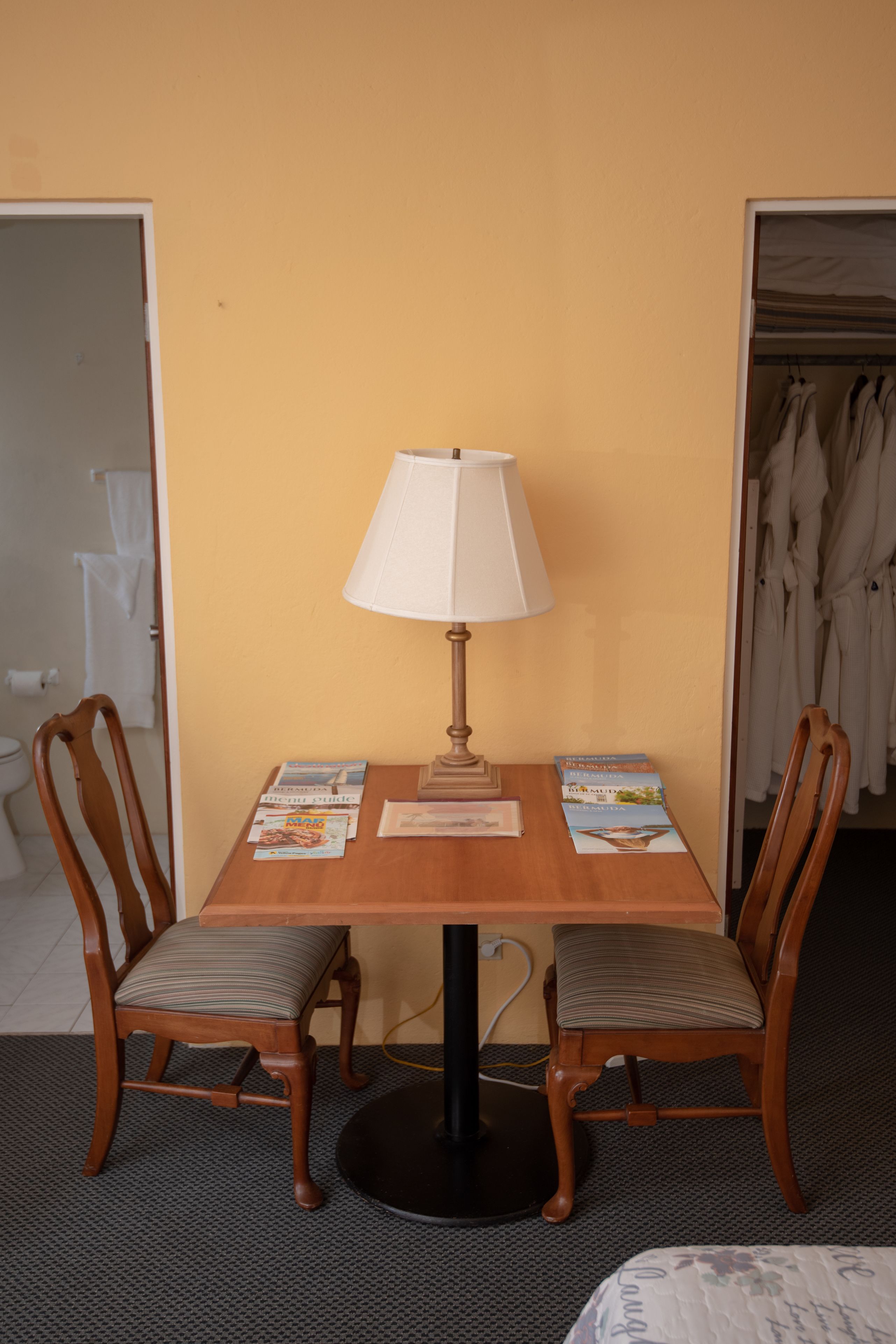 A hotel room with a wooden table, two chairs, a lamp, and a bed.