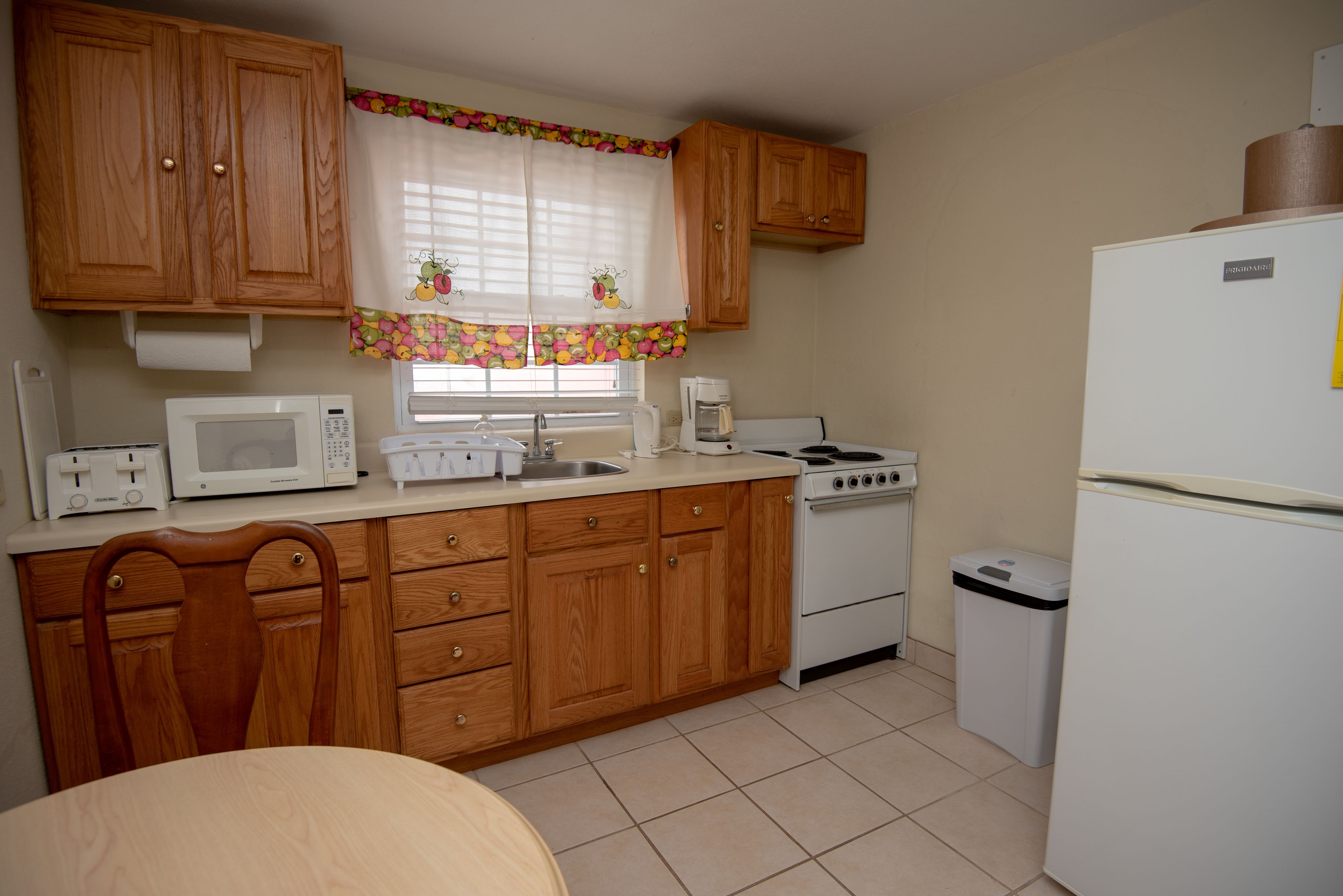A compact kitchen with wooden cabinets, a microwave, stove, sink, and a refrigerator.