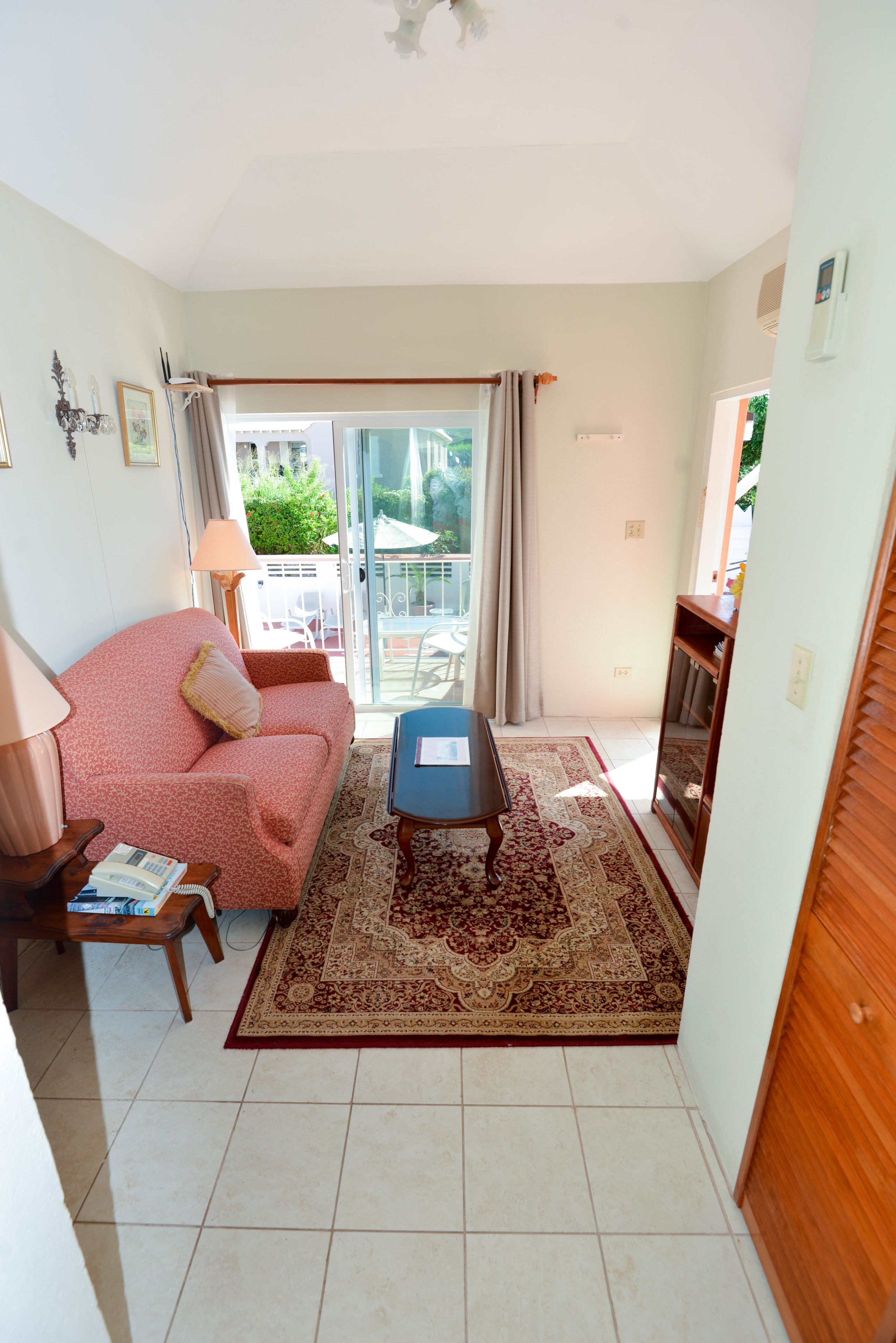 Sala de estar con sofá, una mesita, alfombra y puerta corrediza de vidrio que da a un espacio exterior.