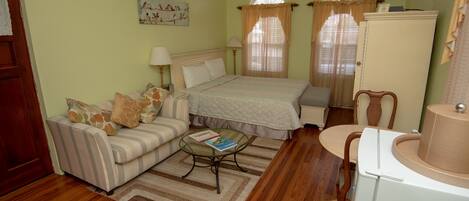 A room with a bed, a sofa, a small table, a chair, a cabinet, and a window with curtains.