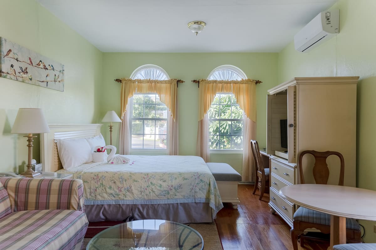 Quarto de hotel com cama, mesa de cabeceira com luminária, cadeira, mesinha, televisão e armário.