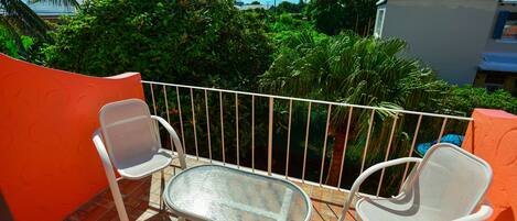 A balcony with two white chairs and a glass table, surrounded by orange walls and a white railing.
