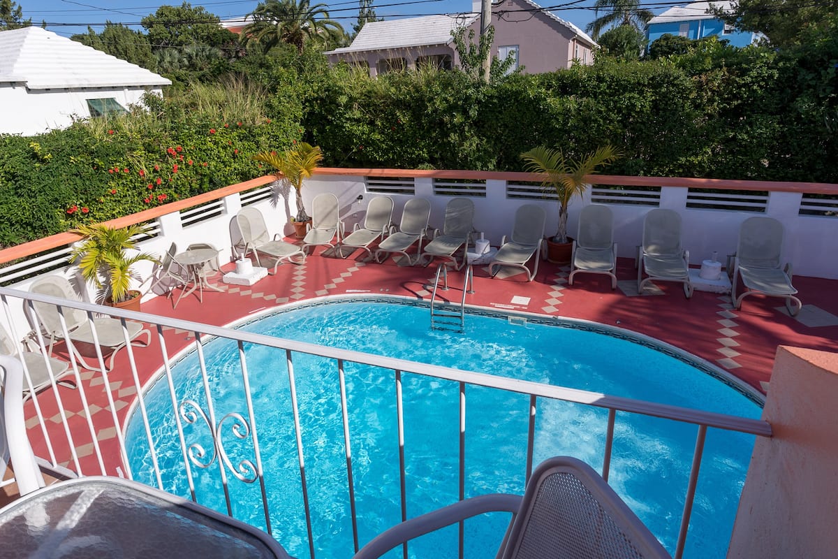 Piscina com deck vermelho, rodeada por espreguiçadeiras e guarda-corpo.