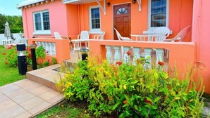 A pink house with a porch, white chairs, and a small garden. - Dawkins Manor Hotel (Paget Parish)