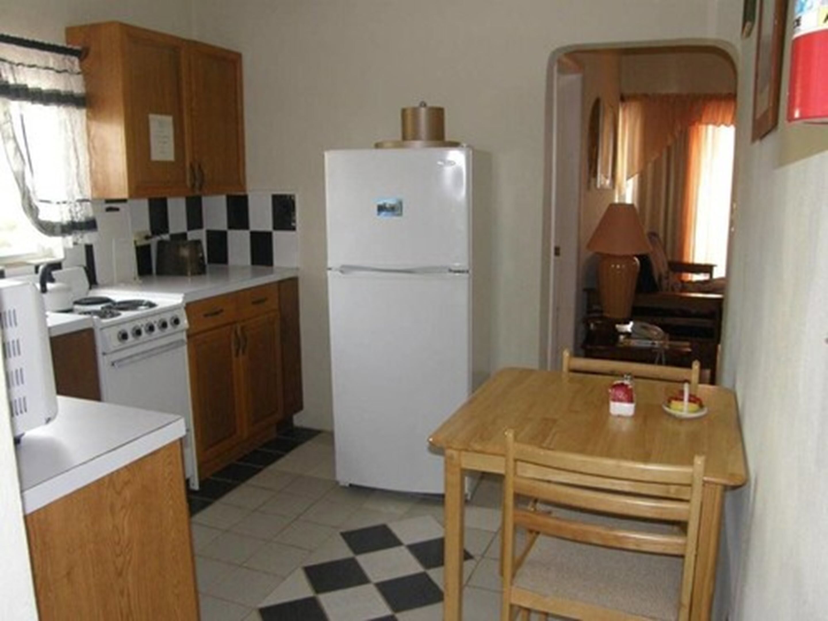 A compact kitchen with wooden cabinets, a white stove, a white refrigerator, and a checkered floor.