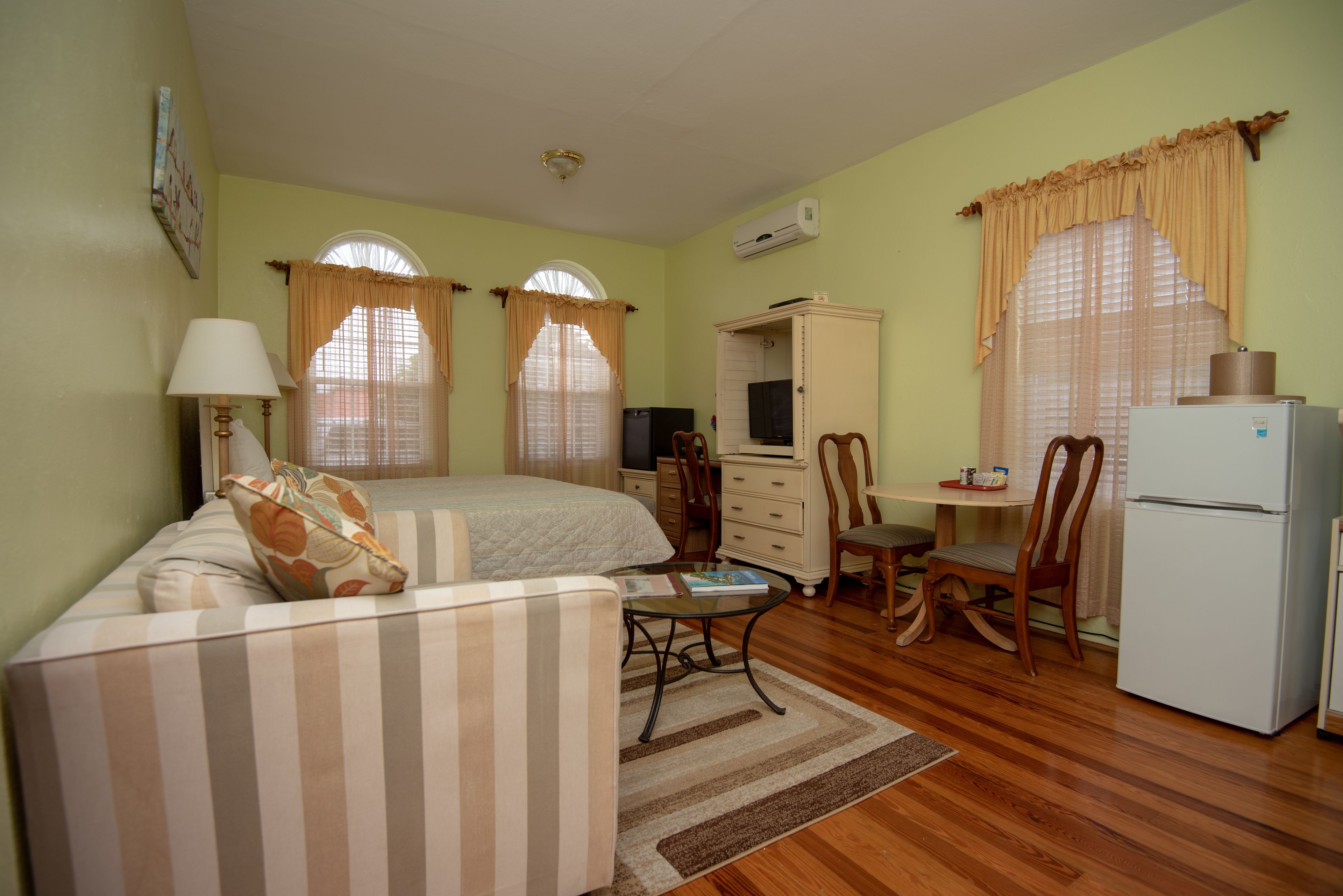 A room with a bed, a sofa, a dining table with chairs, a refrigerator, and an air conditioning unit.