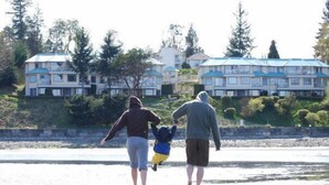 A family walking along a beach with a row of houses in the background. - Ocean Sands Resort (Parksville)