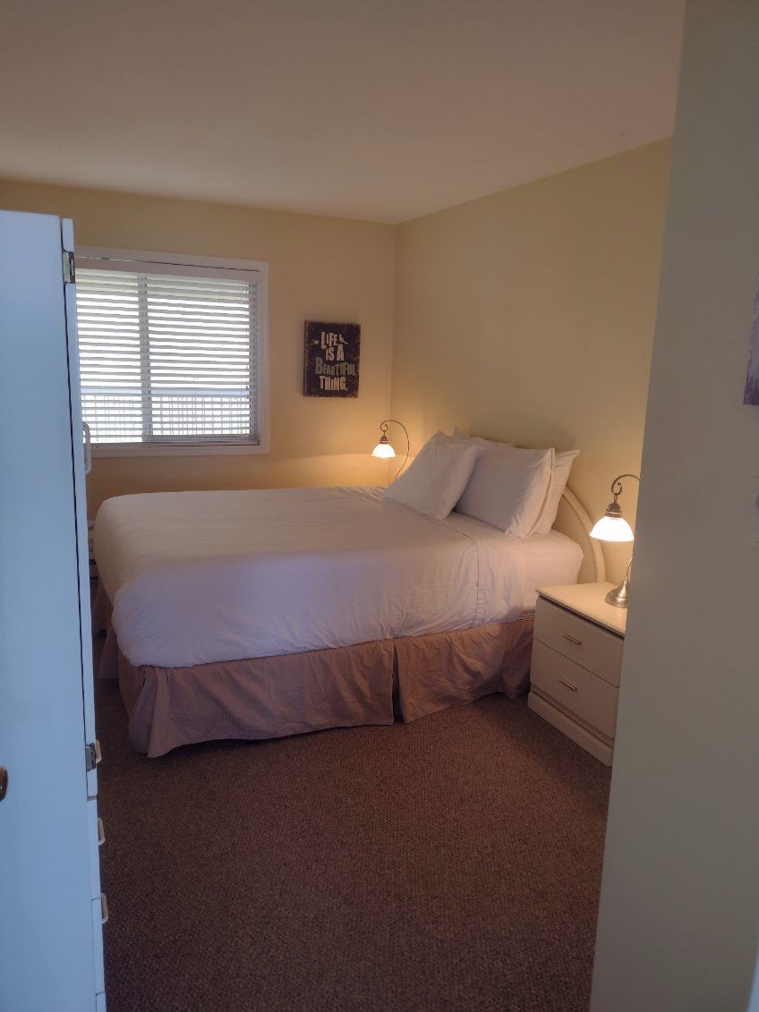 Quarto com cama, abajures, janela com persianas e um letreiro fixado na parede.