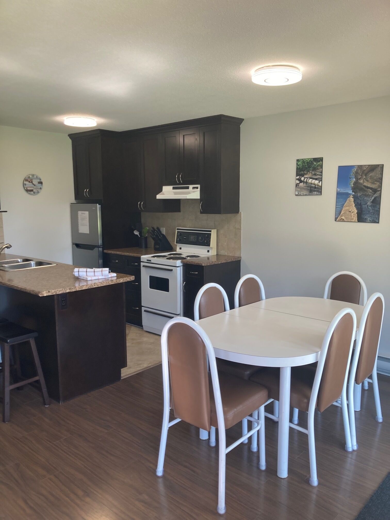 A modern kitchen with dark cabinets, a central island with a sink, and a dining area with six chairs.