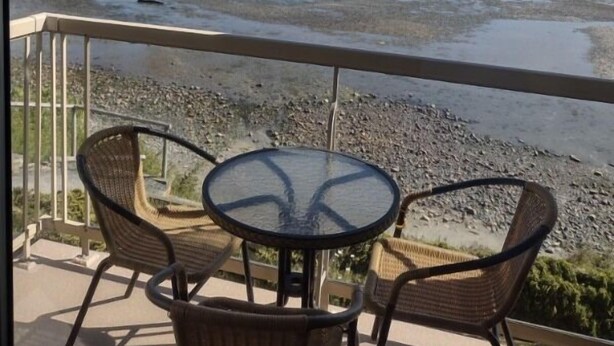 A balcony with wicker chairs and a glass table overlooking a salt flat with distant mountains. - Ocean Sands Resort (Parksville)