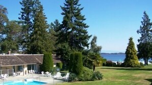A pool area with lounge chairs, a building with a sloped roof, and a view of the sea. - Ocean Sands Resort (Parksville)