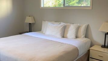 A bedroom with a large bed, a nightstand, a lamp, and a window with a view of trees.