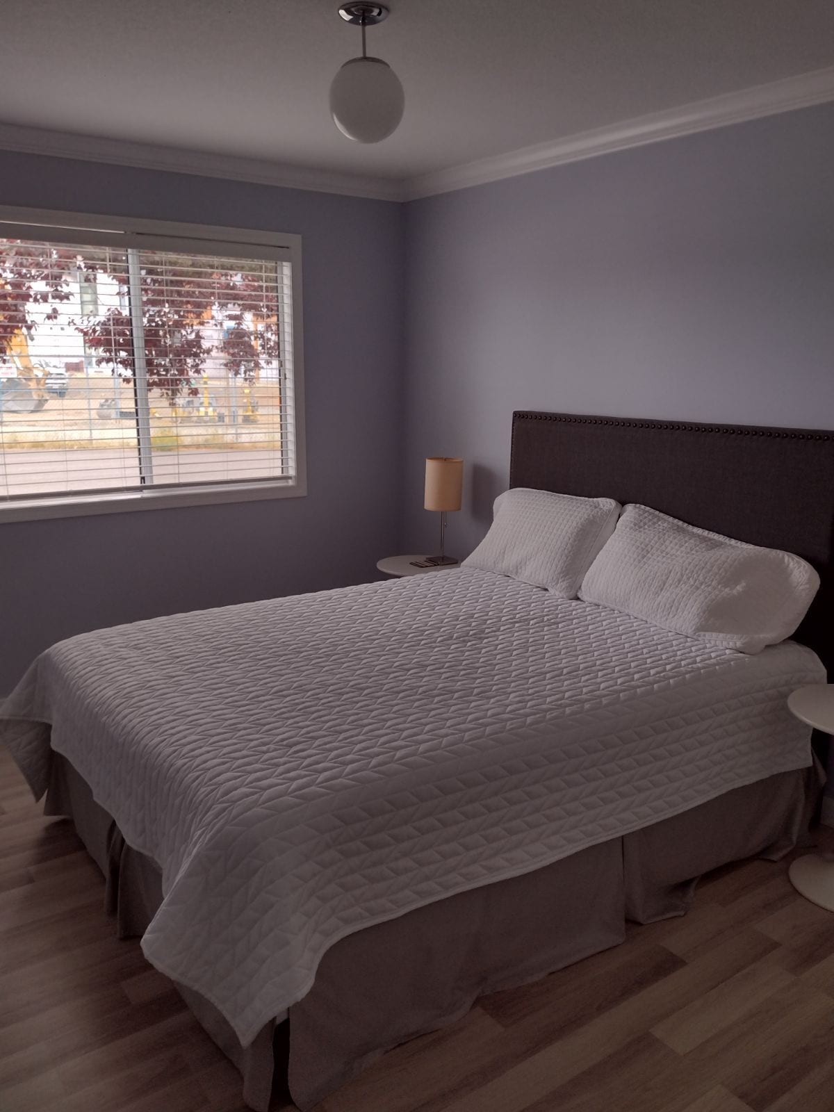A bedroom with a bed, a nightstand, a lamp, and a window with blinds.