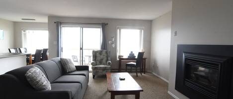 A living room with a sofa, armchair, coffee table, fireplace, and large windows.