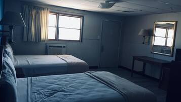 A hotel room with two beds, a desk, a chair, a window with curtains, an air conditioning unit, and a door.