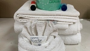 A stack of white towels with a teal roll of toilet paper and a small bottle on top.