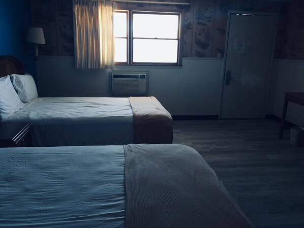 Una habitación con dos camas, una ventana con cortinas, un radiador y una puerta.