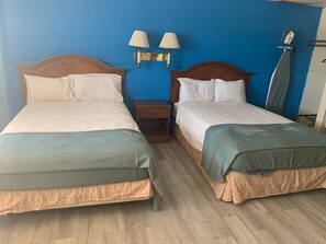 A hotel room with two beds, wooden headboards, and a nightstand with lamps.