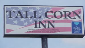 A billboard for Tall Corn Inn, featuring an American flag design with text highlighting amenities like reasonable rates, clean rooms, free breakfast, internet, and cable TV.