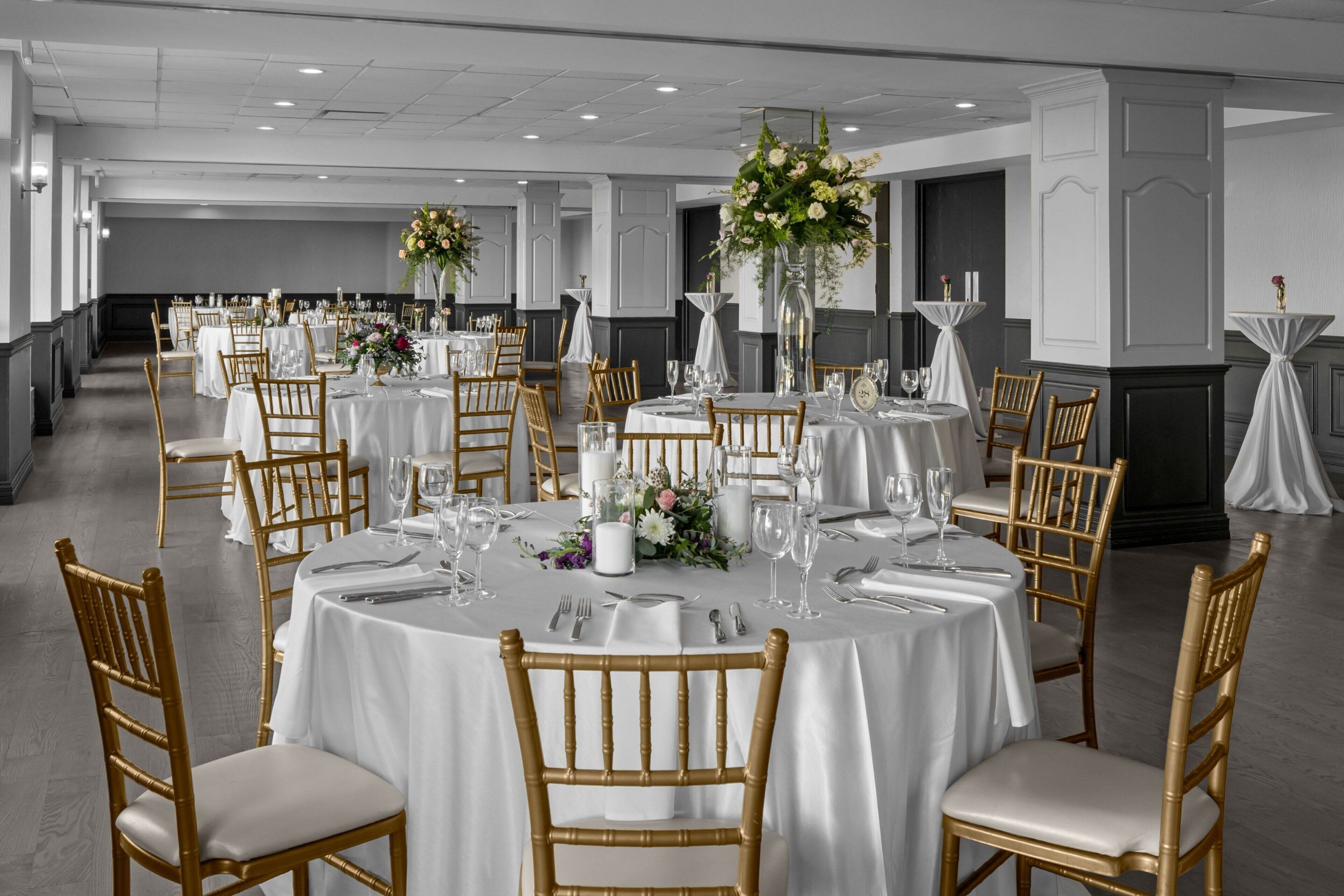 A banquet hall with round tables, white tablecloths, and gold chairs.