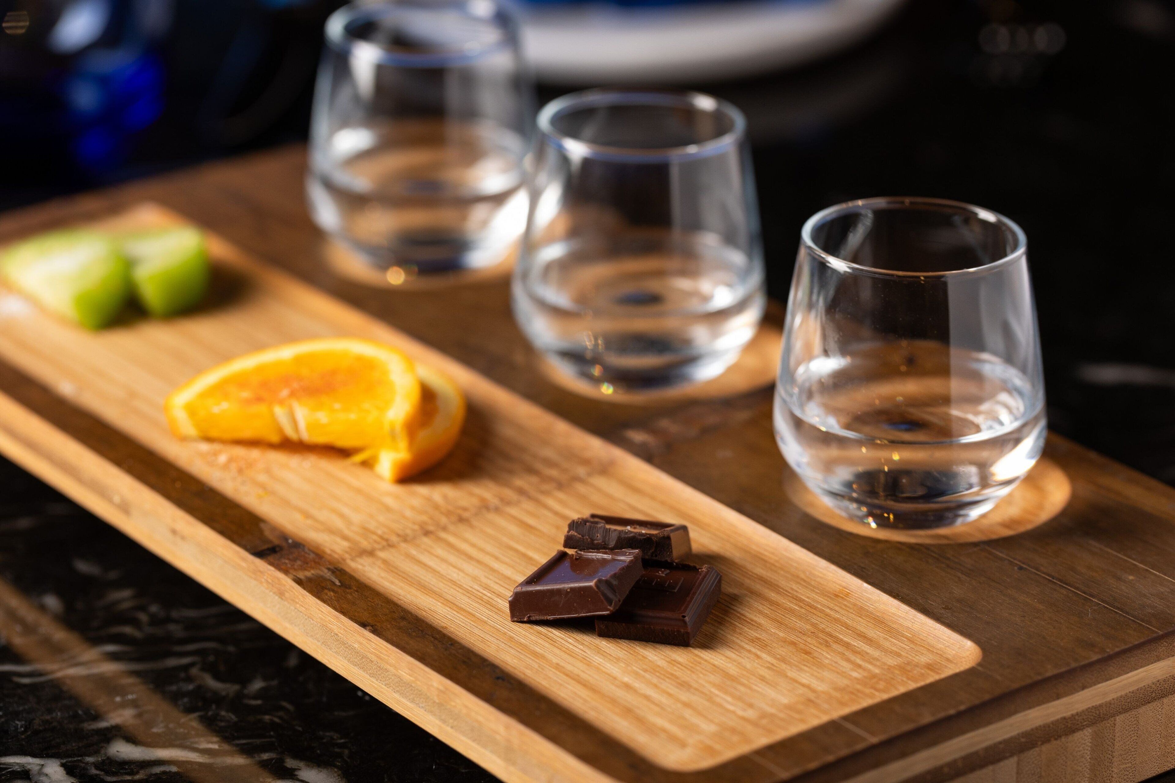 Una tabla de madera con rodajas de naranja, trozos de chocolate y vasos vacíos.