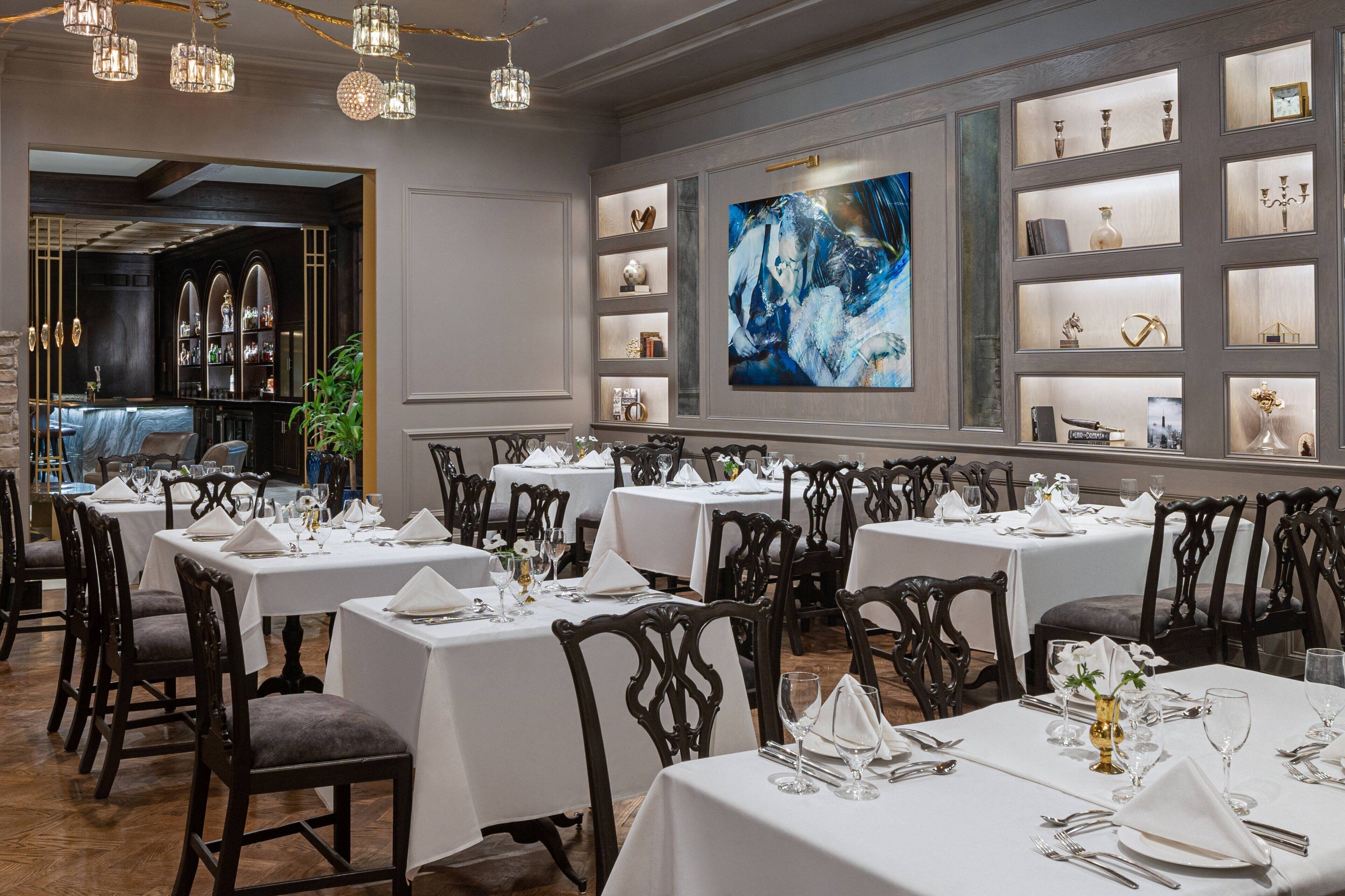 Un restaurant avec plusieurs tables dressées pour le service, un coin bar et un mur orné d’étagères où sont exposés divers objets.