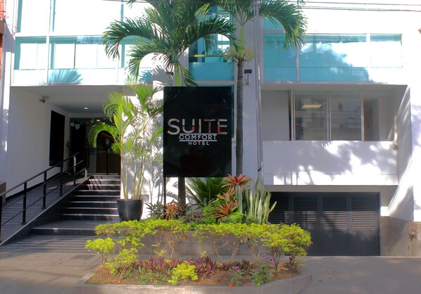 A hotel entrance with a sign reading "SUITE COMFORT HOTEL," a staircase, and a variety of potted plants.