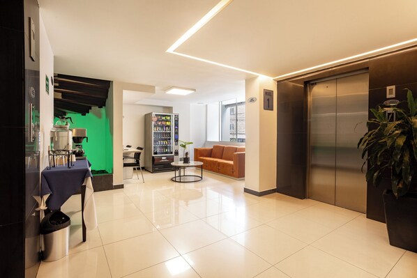 A modern lobby with a coffee machine, seating area, vending machine, and an elevator. - Hotel Suite Comfort (Medellín)