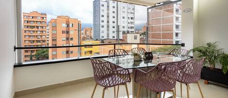 A balcony with a glass table and chairs, a potted plant, and a city view.