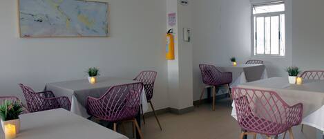 A dining area with tables and chairs, a fire extinguisher, a wall-mounted phone, and a window with blinds.