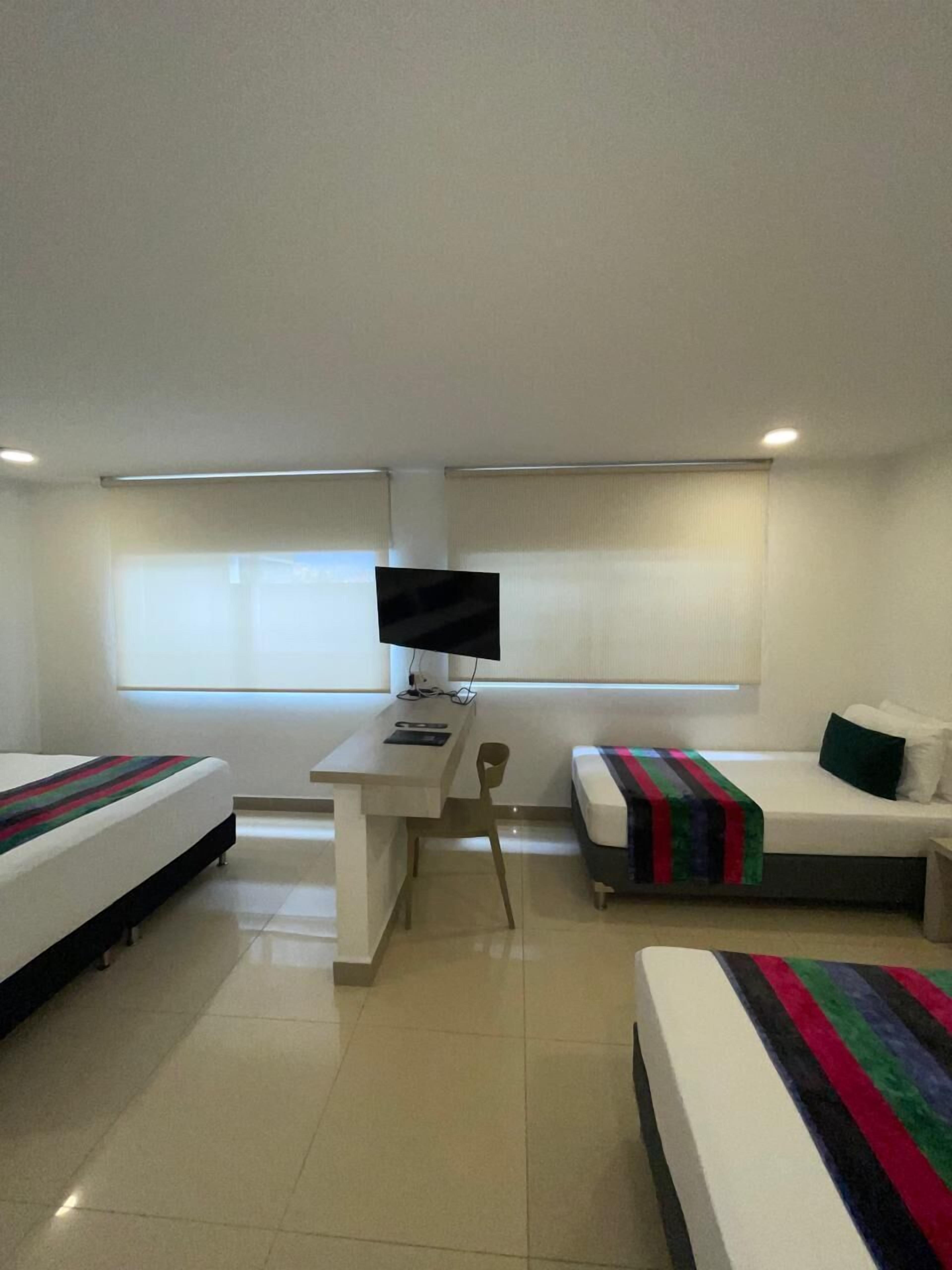 A hotel room with two beds, a desk, a chair, a television, and a window.