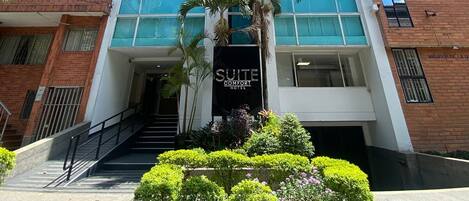 Un hotel moderno con fachada de vidrio, un llamativo letrero 'SUITE COMFORT HOTEL' y un jardín bien cuidado al frente.