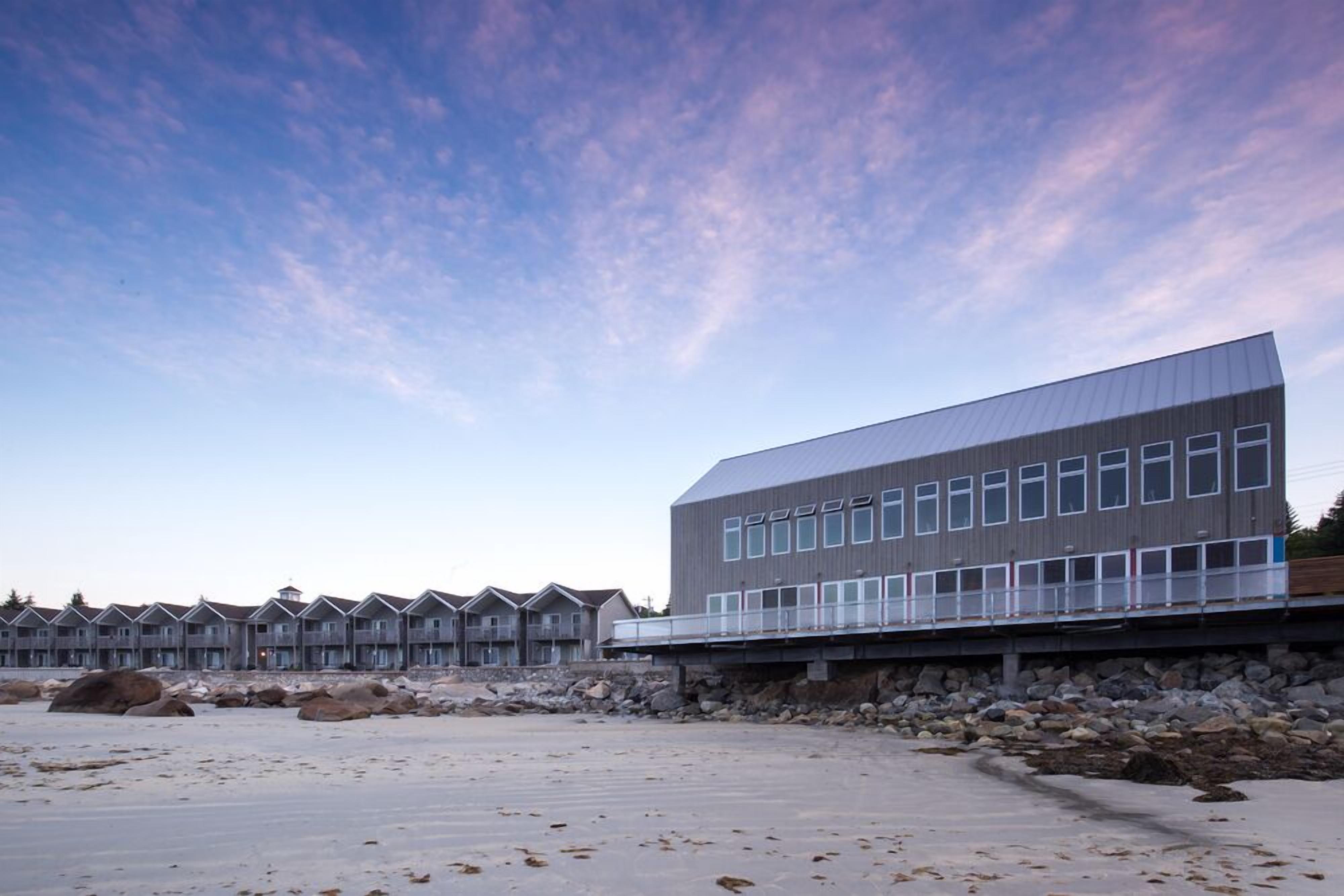 A modern building with a flat roof and multiple windows, situated next to a rocky shoreline.