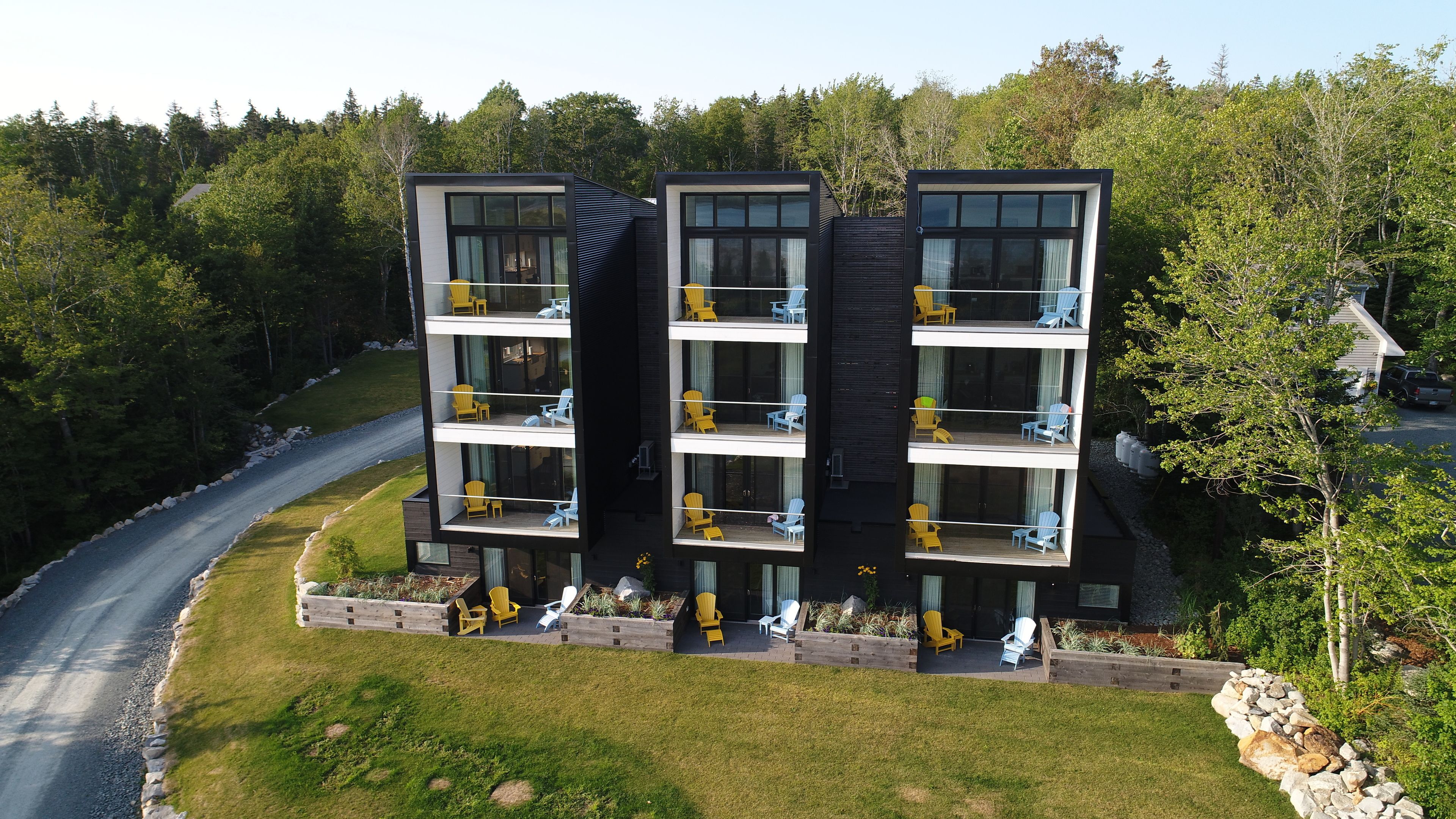 Un immeuble moderne à plusieurs étages, doté de balcons et entouré d’une zone boisée.