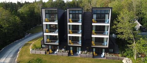 A modern multi-story building with balconies, surrounded by a forested area.