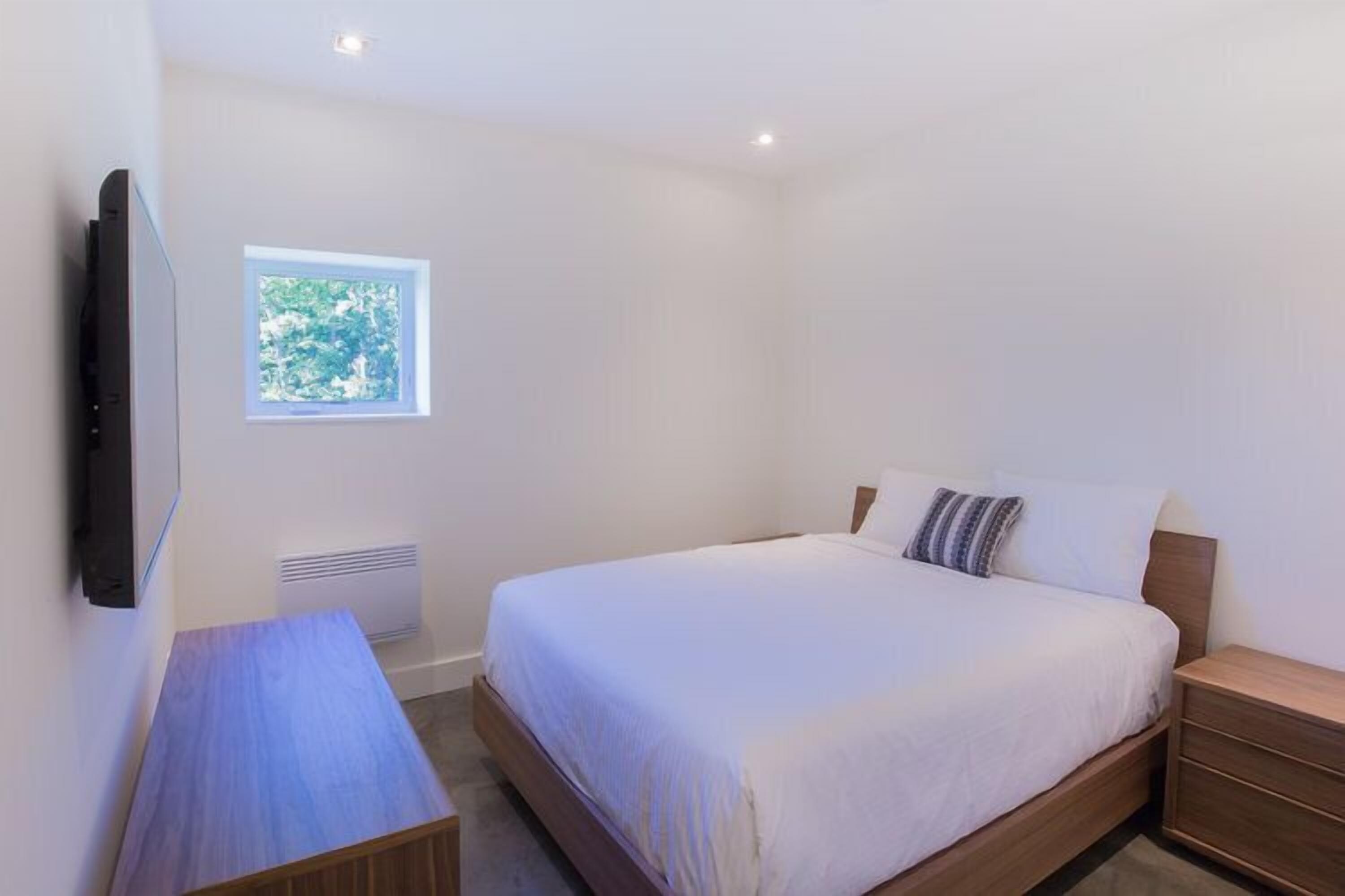 Un dormitorio con cama, mesita de noche y televisor montado en la pared.