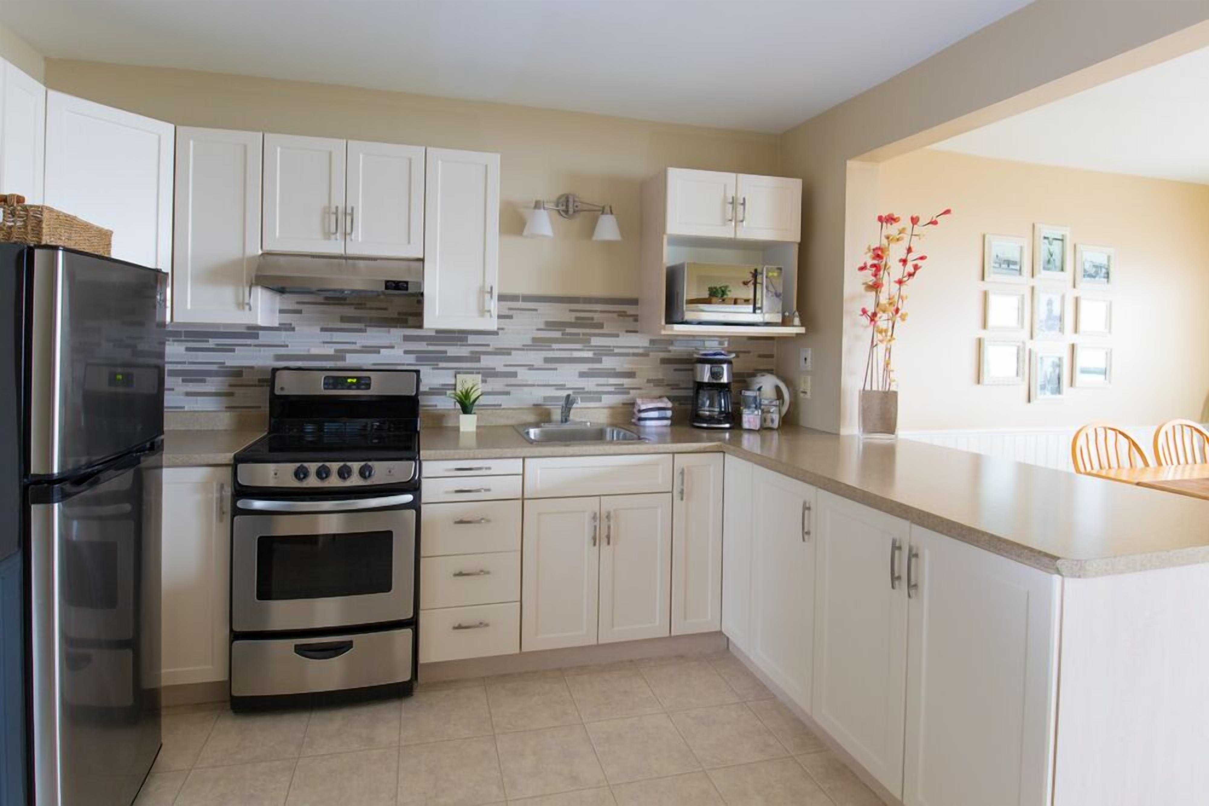 A modern kitchen with white cabinets, stainless steel appliances, a tiled backsplash, and a dining area with a vase of flowers.