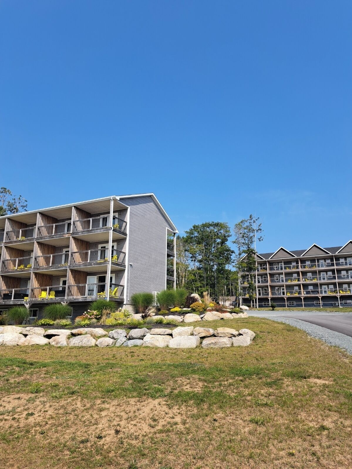 Ein mehrstöckiges Hotel mit Balkonen, ein angelegter Garten mit Steinen und Pflanzen und einem strahlend blauen Himmel.