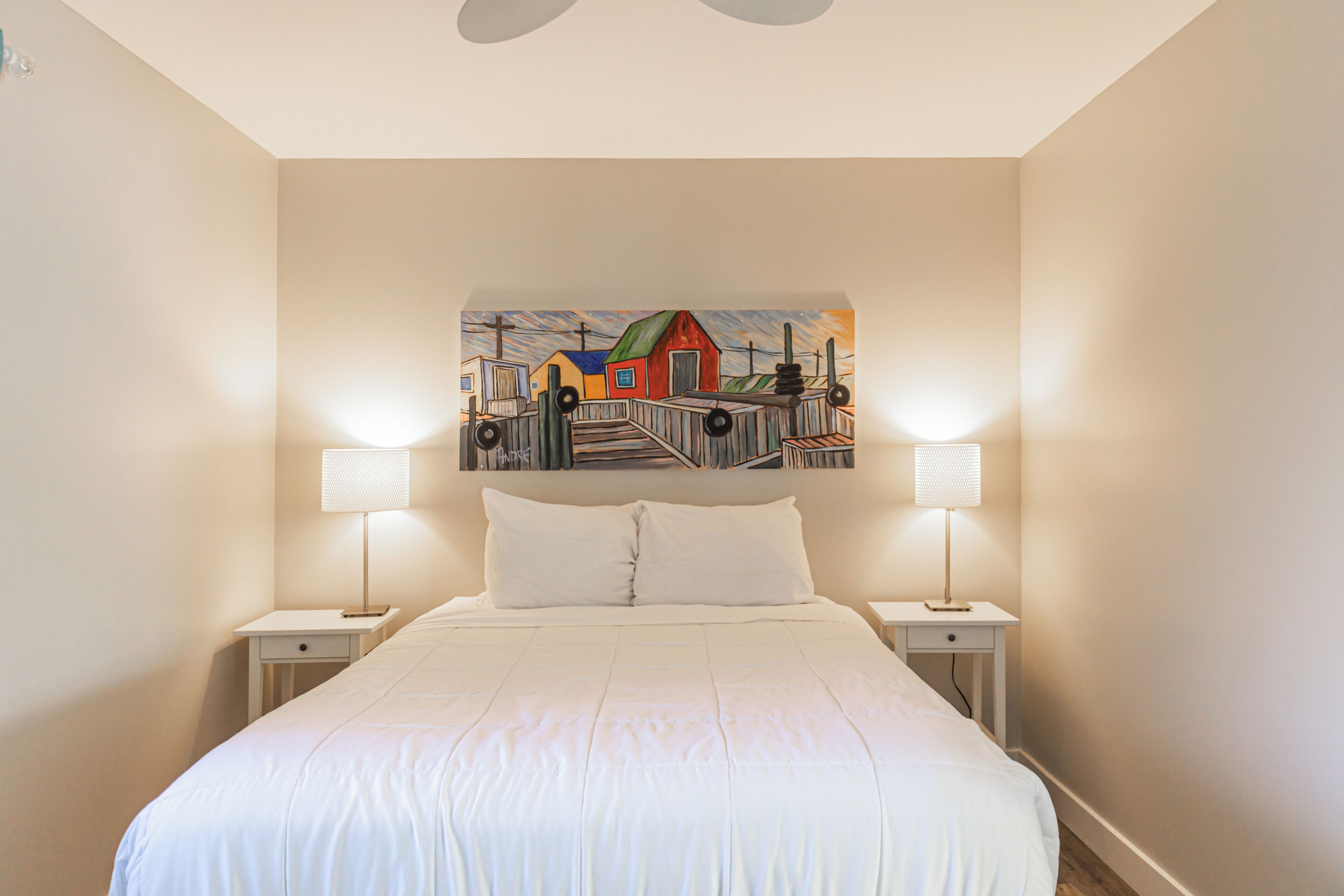 Un dormitorio con una cama grande, dos mesitas de noche con lámparas y un cuadro colorido en la pared.