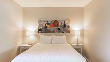Un dormitorio con una cama grande, dos mesitas de noche con lámparas y un cuadro colorido en la pared.