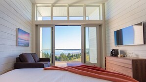A modern bedroom with a large bed, a sofa, a TV, and a view of the outdoors. - The Quarterdeck Resort (Summerville Centre)