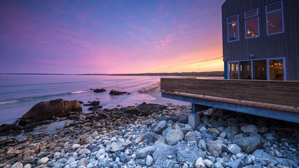 A modern building with a wooden deck overlooking a rocky shoreline. - The Quarterdeck Resort (Summerville Centre)